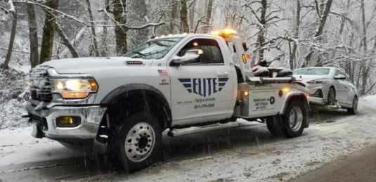 Elite Towing & Recovery truck towing a car on a snowy road